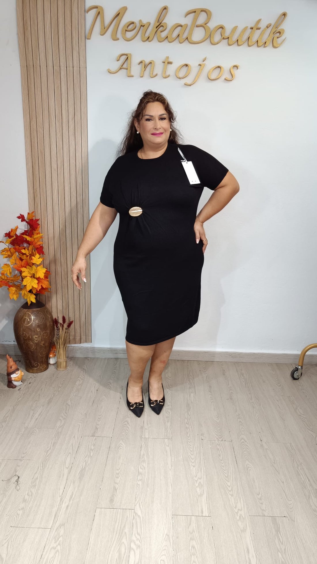 Vestido Venecia negro de manga corta con fruncido delantero y adorno ovalado dorado, llevado por modelo.