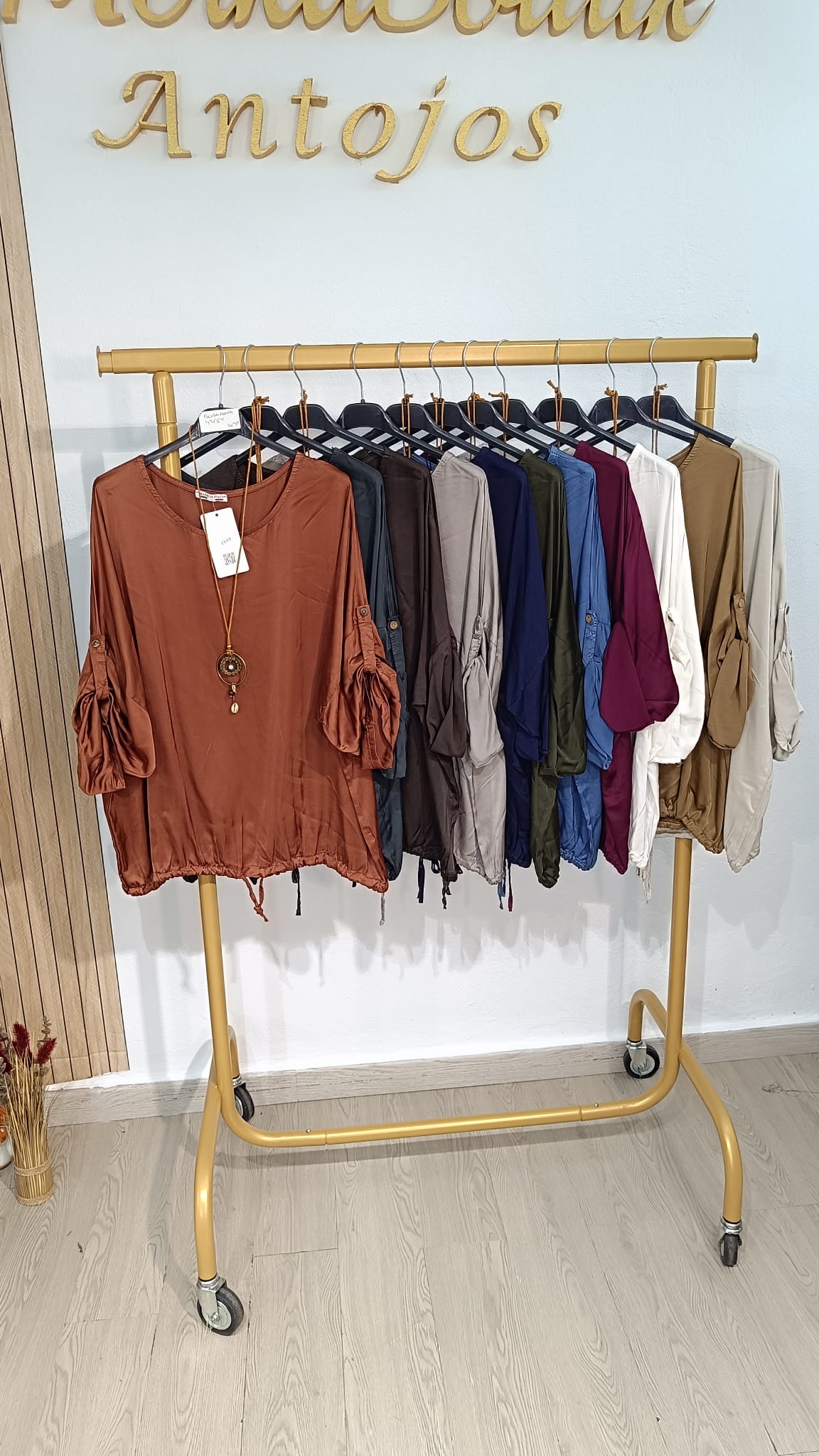 Blusa Satén Roma de corte holgado y mangas amplias con frunces, expuesta en varios colores en perchero