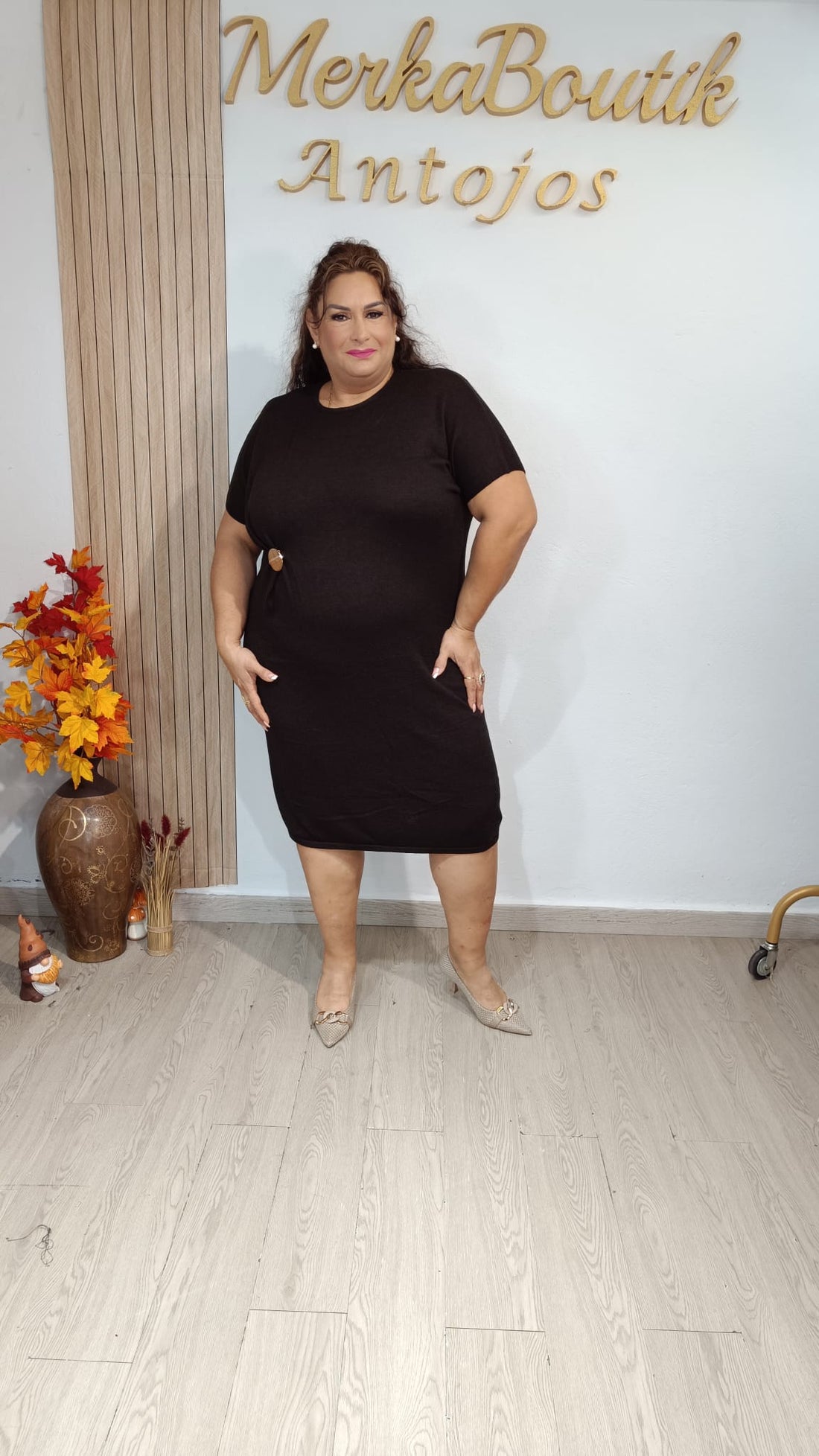 Vestido Venecia negro de manga corta con fruncido delantero y adorno ovalado dorado, llevado por modelo.