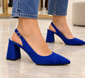 Zapato Lucía azulón de punta fina y tacón ancho con hebilla dorada en los pies de una modelo